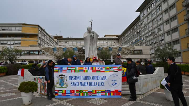Faithfuls, priests and nuns hold a banner which reads, "Latin American Mission, Holy Mary of the Light", as they pray at the statue of John Paul II outside the Gemelli University Hospital where Pope Francis is hospitalised in Rome on 15 March 2025. Pope Francis marked a month in hospital on 14 March 2025, with football players sending him messages of support for his recovery from pneumonia, including the captain of his favorite team, San Lorenzo.