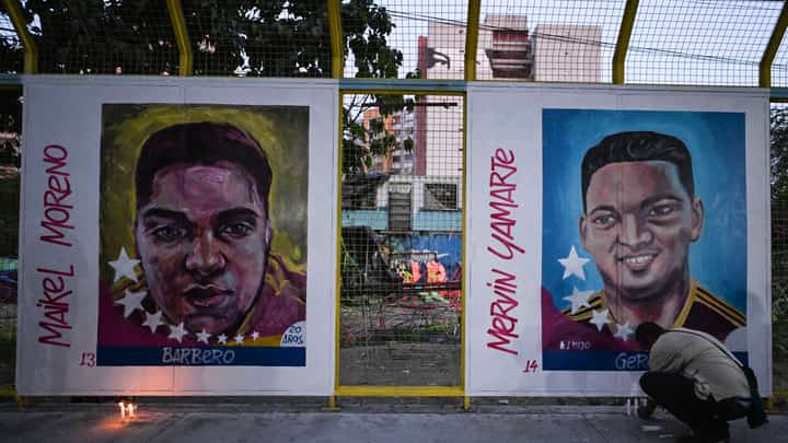 A man lights a candle in front of paintings of Venezuelan migrants deported from the US to a maximum security prison in El Salvador during a vigil in front of El Salvador embassy in Caracas on 2 April 2025.