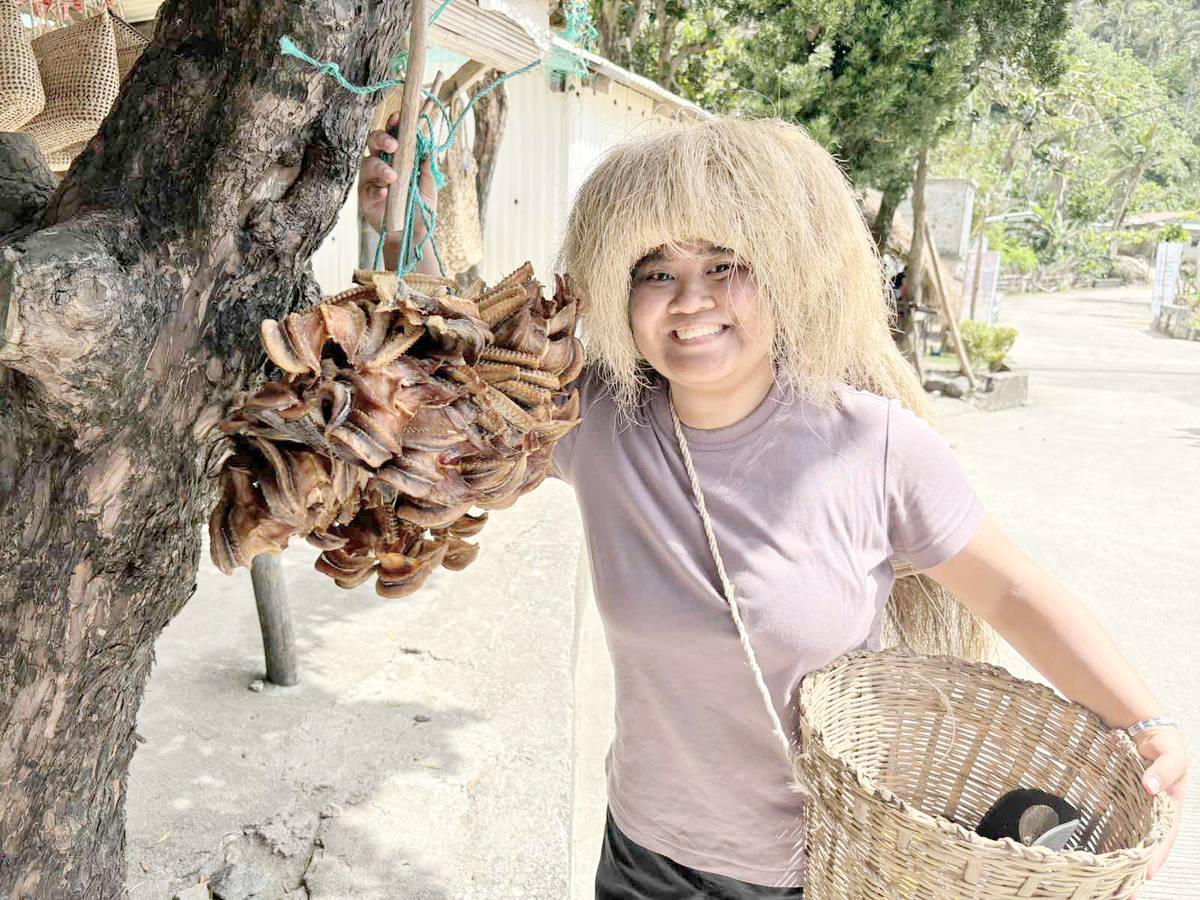 Kyla Valdez of DoT communications office wears the traditional headdress ‘vakul’ in Chavayan Village. She also shows dried ‘dorado,’ a considered gem fish in Batanes as it costs P1,200 per kilo.