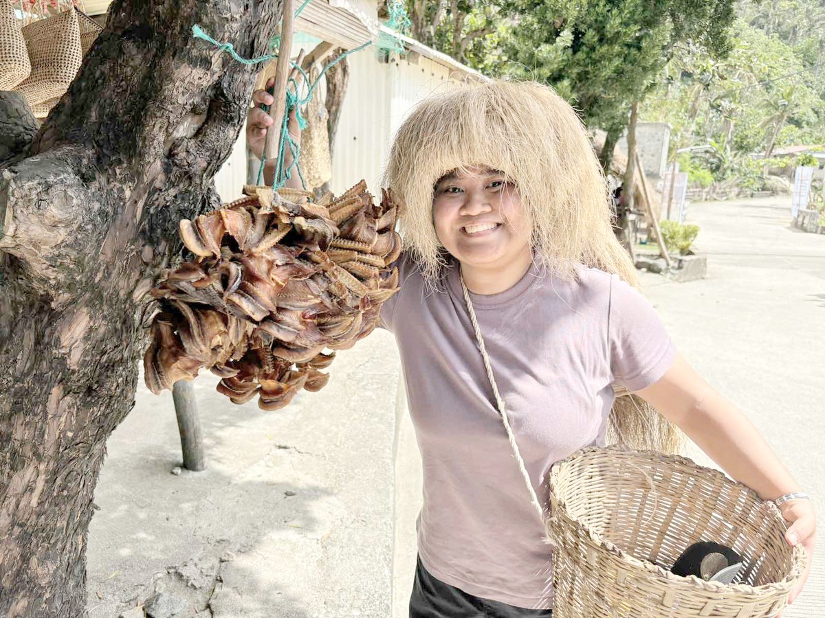 Kyla Valdez of DoT communications office wears the traditional headdress ‘vakul’ in Chavayan Village. She also shows dried ‘dorado,’ a considered gem fish in Batanes as it costs P1,200 per kilo.