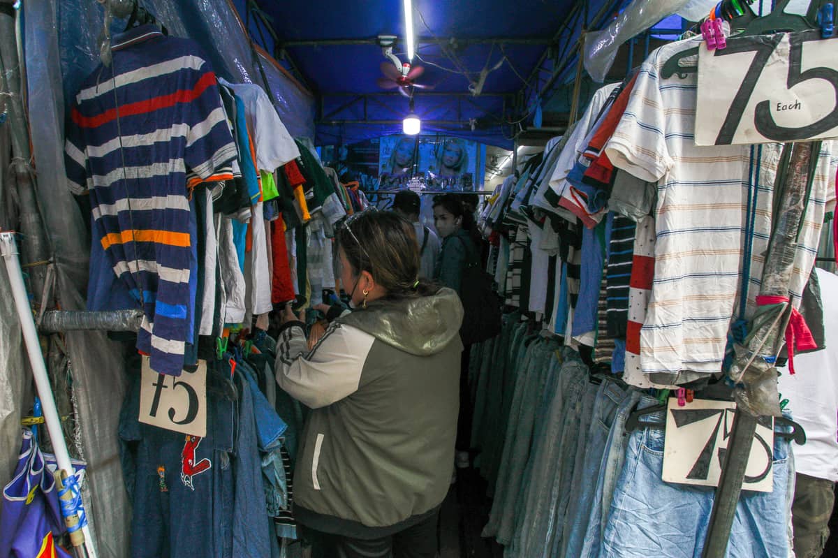 Shoppers browse through racks of secondhand clothes at an ukay-ukay stall in the Philippines, where shirts and jeans are sold for as low as ₱75. Amid rising clothing waste globally, affordable thrift shops like this continue to thrive.