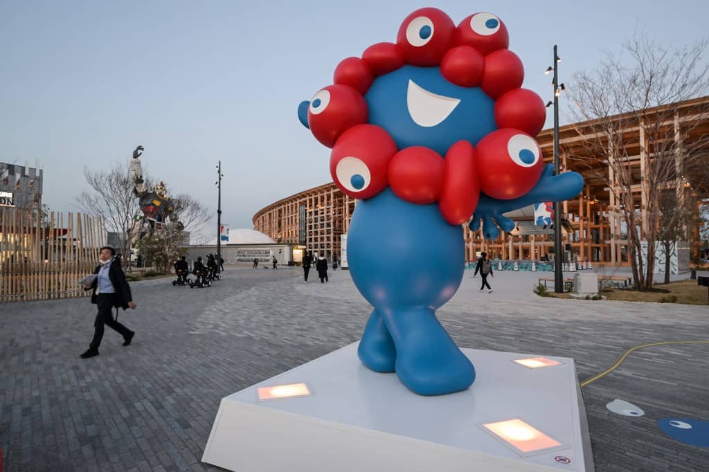A man (L) walks past "Myaku-Myaku", the mascot of the 2025 Osaka Expo, during a media preview day for the expo in the city of Osaka on 9 April 2025, four days before the event opens to the public for six months.