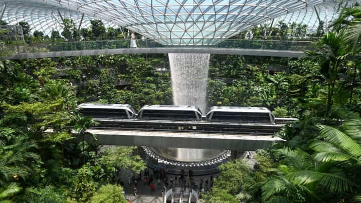 A WOMAN (top) walks across the bridge next to the Rain Vortex, the world's tallest indoor waterfall, and a mono-rail train going through the Jewel Complex at Singapore Changi Airport in Singapore on 10 April 2025.