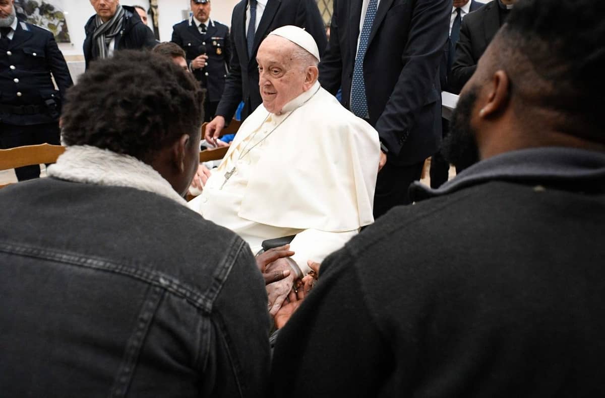 Pope Francis smiles and clasps the hand of an inmate seated before him, while others look on during his Holy Thursday visit to Regina Coeli Prison.