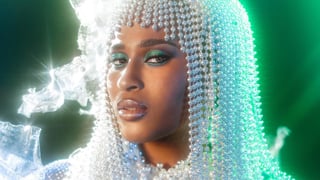 A close-up portrait of Alexie Brooks wearing a headpiece made of shimmering pearls, with green eyeshadow and glossy lips.