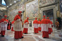 Catholic cardinals dressed in red vestments walk solemnly through a fresco-lined corridor toward the Sistine Chapel as they prepare to enter the papal conclave.