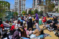 Crowds of Istanbul residents, including families with children, gather in a park during daylight after evacuating buildings due to a 6.2-magnitude earthquake, with people sitting on blankets and holding babies amid apartment buildings in the background.