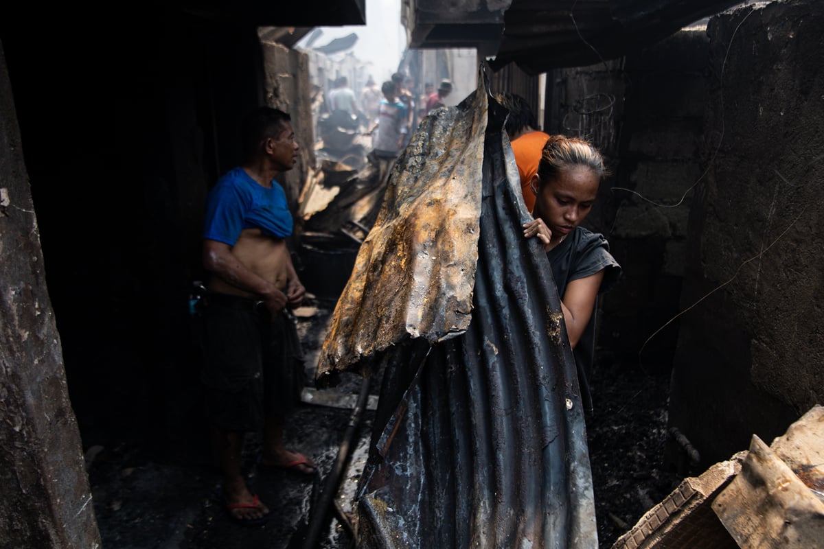 A resident carries the metal roofing from her burned-down house after a massive fire. She plans to sell the remaining scraps to help recover from the disaster.