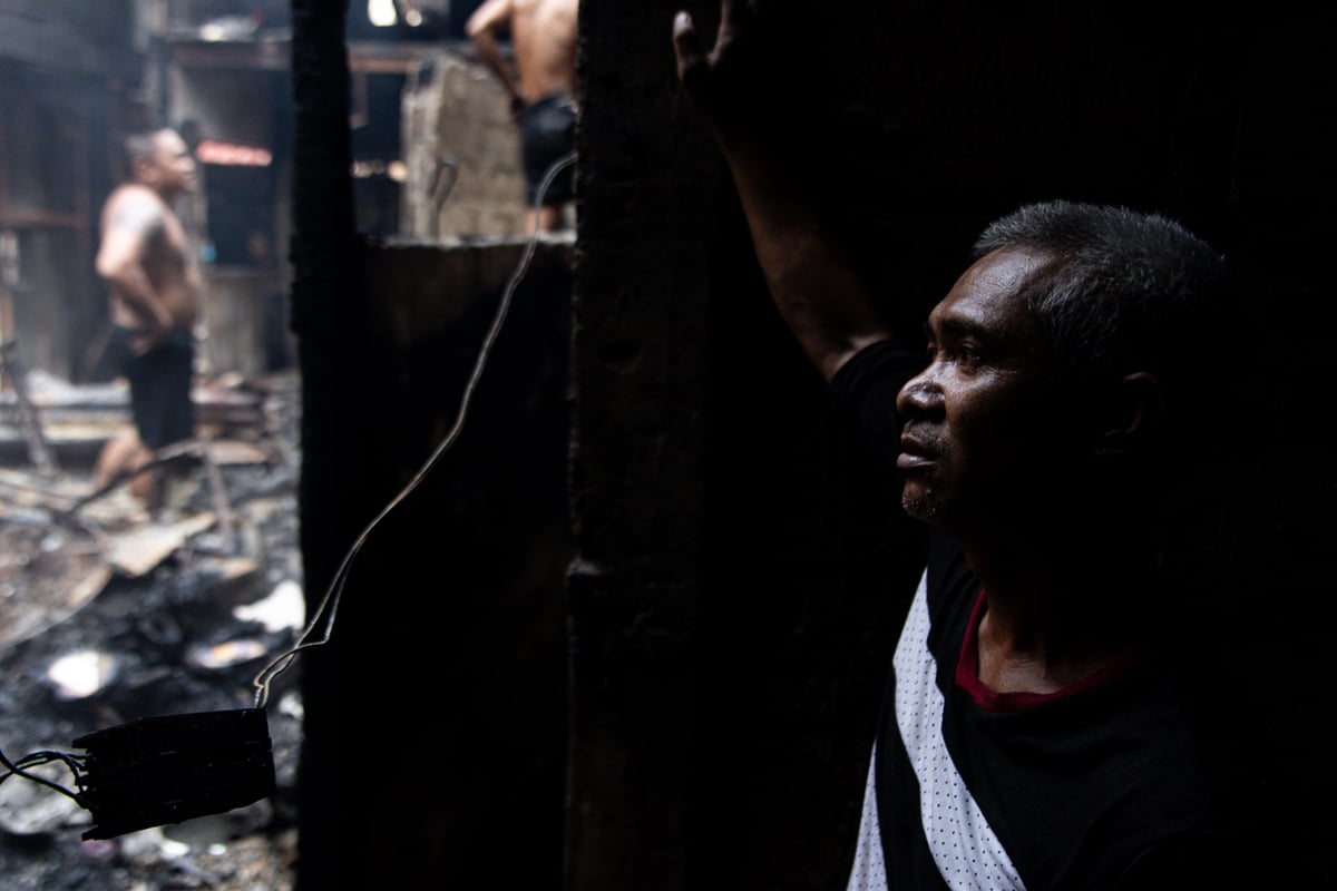 A resident stares at his burned-down house as he takes a break from salvaging what little remains. He said he is considering leaving the community, as this is the fourth time their neighborhood has been hit by fire.
