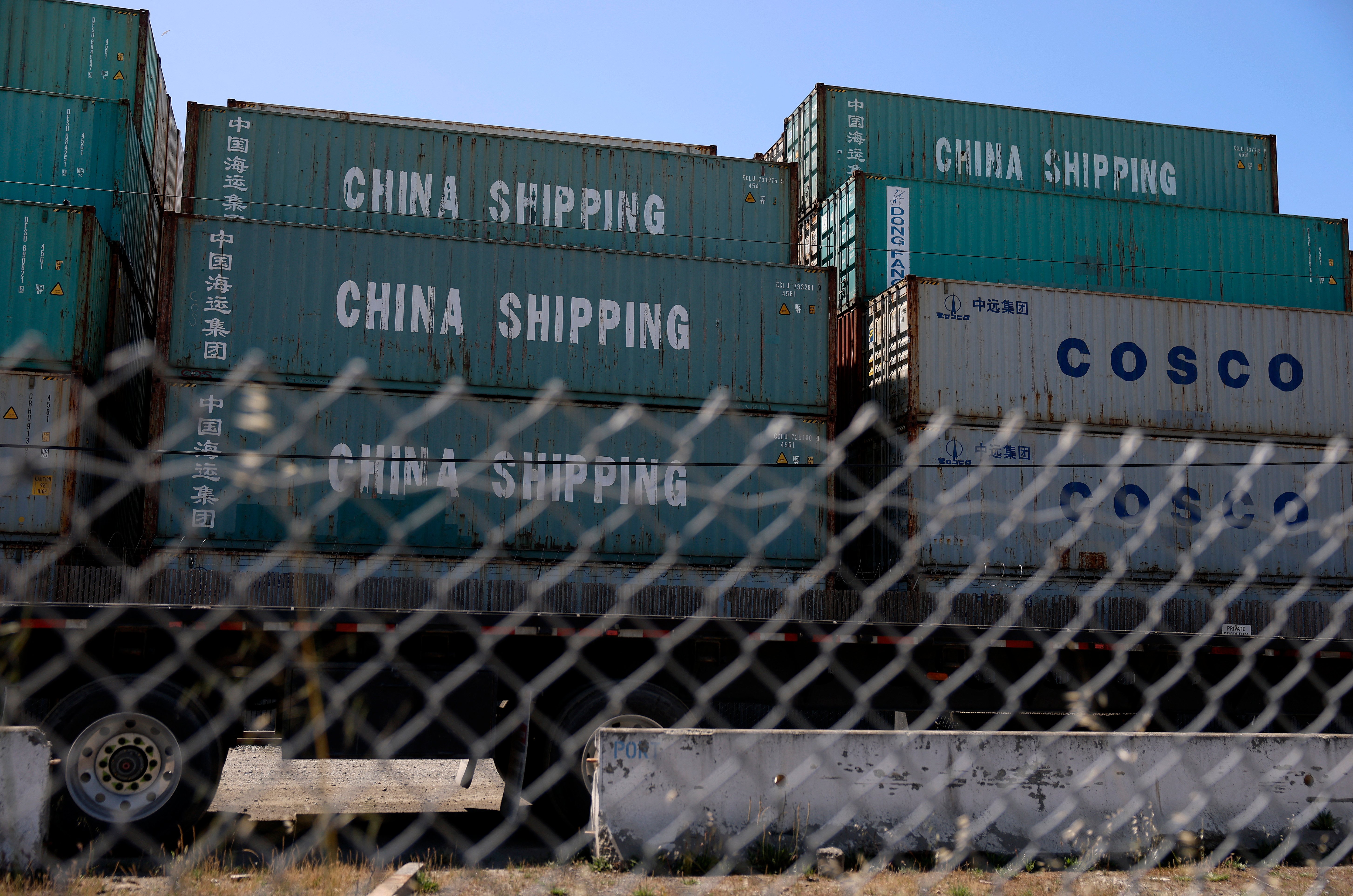 Shipping containers labeled "China Shipping" and "COSCO" are stacked behind a chain-link fence at the Port of Oakland, California, on 28 April 2025, amid a surge in canceled sailings from China due to ongoing U.S. tariffs.