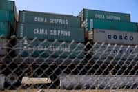Shipping containers labeled "China Shipping" and "COSCO" are stacked behind a chain-link fence at the Port of Oakland, California, on 28 April 2025, amid a surge in canceled sailings from China due to ongoing U.S. tariffs.