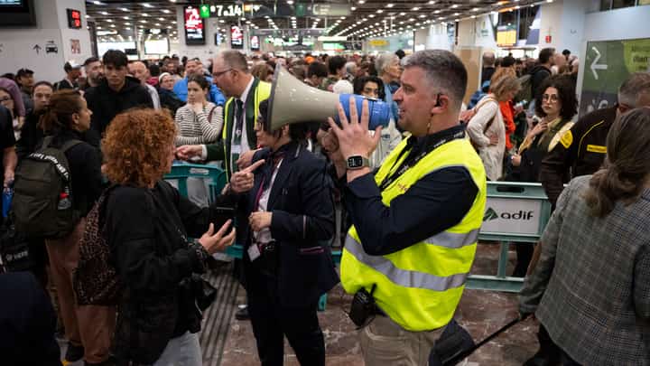 An employee of Spanish state-owned rail company RENFE speaks into a megaphone to share information as passengers wait before boarding their train at Sants railway station in Barcelona on 29 April 2025, a day after a massive power cut affecting the entire Iberian peninsula and the south of France.