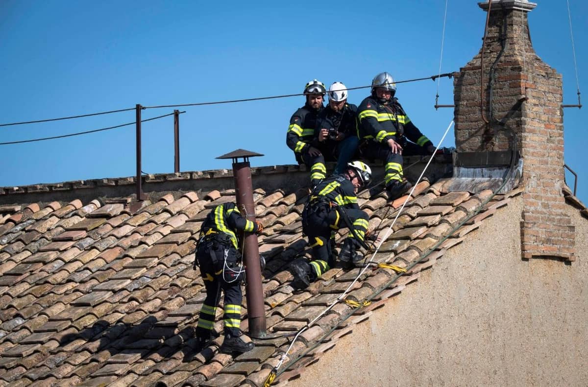 Firefighters work atop the Sistine Chapel, securing the chimney where smoke will signal the outcome of each conclave vote—white for a new pope, black if no decision.