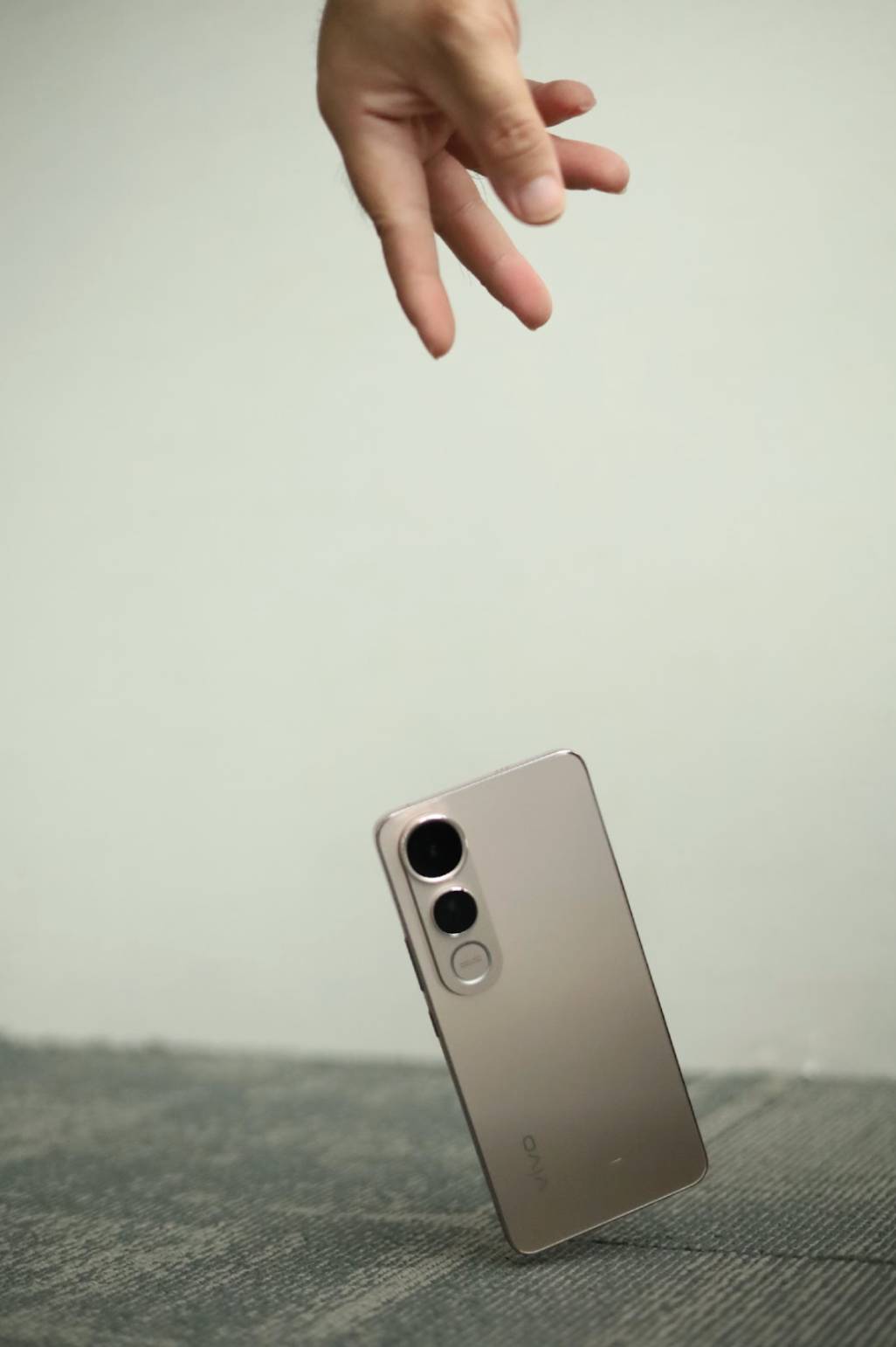 A hand releasing a vivo V50 Lite smartphone mid-fall as it lands on a cushioned surface, demonstrating the phone’s durable construction and impact resistance.