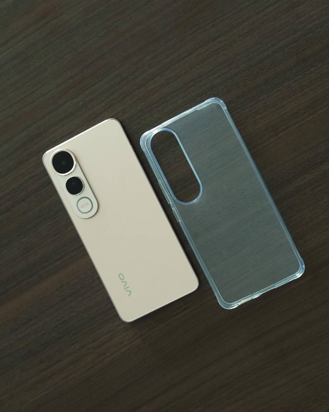 A vivo V50 Lite smartphone laid beside its transparent shock-resistant case on a dark wooden surface, showcasing the device’s sleek design and included protective gear.