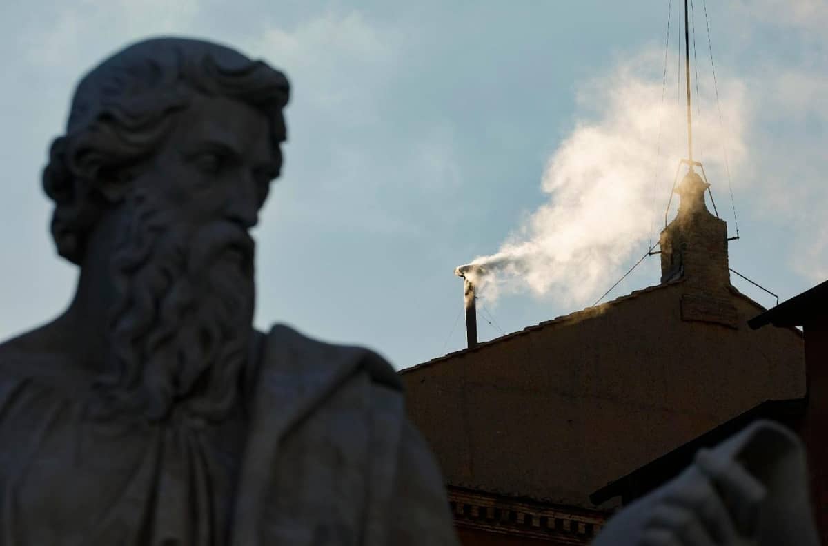 White smoke rises from the chimney of the Sistine Chapel in Vatican City on 8 May 2025, signaling the election of a new pope. A statue of a bearded saint is seen in the foreground.