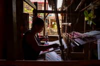 An Inabel weaver works on a handloom inside a traditional workshop in Ilocos Norte, weaving red and blue silhouettes into fabric that forms the official logo of Palarong Pambansa 2025.