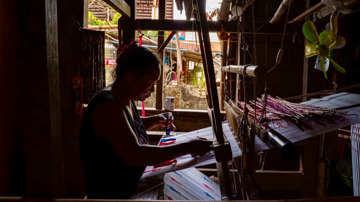 An Inabel weaver works on a handloom inside a traditional workshop in Ilocos Norte, weaving red and blue silhouettes into fabric that forms the official logo of Palarong Pambansa 2025.