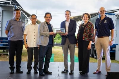U.S. and Philippine officials pose together during the turnover of mobile energy systems in Puerto Princesa, with Ambassador MaryKay Carlson and other dignitaries holding a miniature MES model in front of two parked solar-powered trailers.
