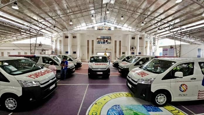 Seven white PCSO-labeled Patient Transport Vehicles are parked inside the Davao Oriental provincial capitol covered court, part of a donation to improve emergency medical services in the region.