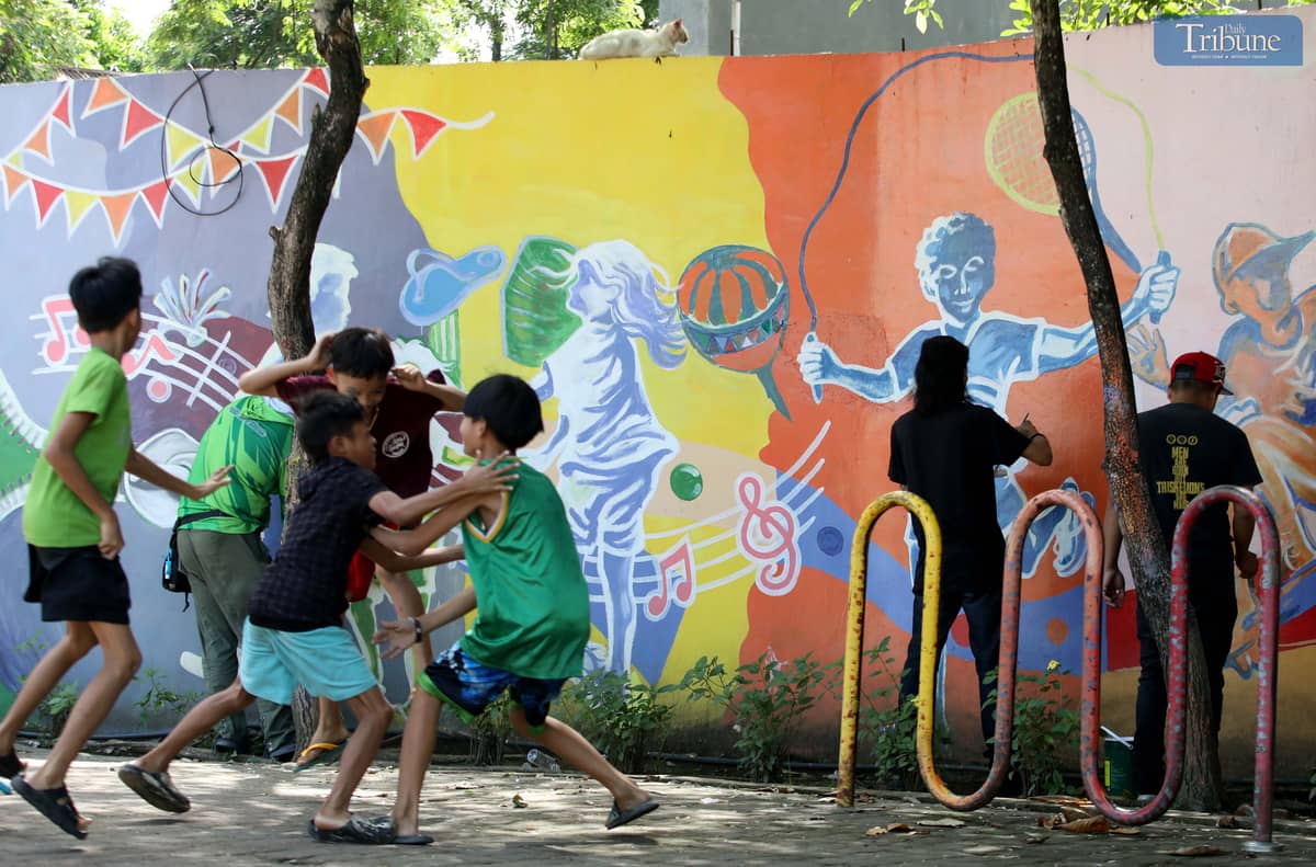Children play nearby as a visual artist adds the finishing touches to a colorful mural at Sambag in Jaro District, Iloilo City. The artwork transforms the wall into a playful, vibrant space for the community.