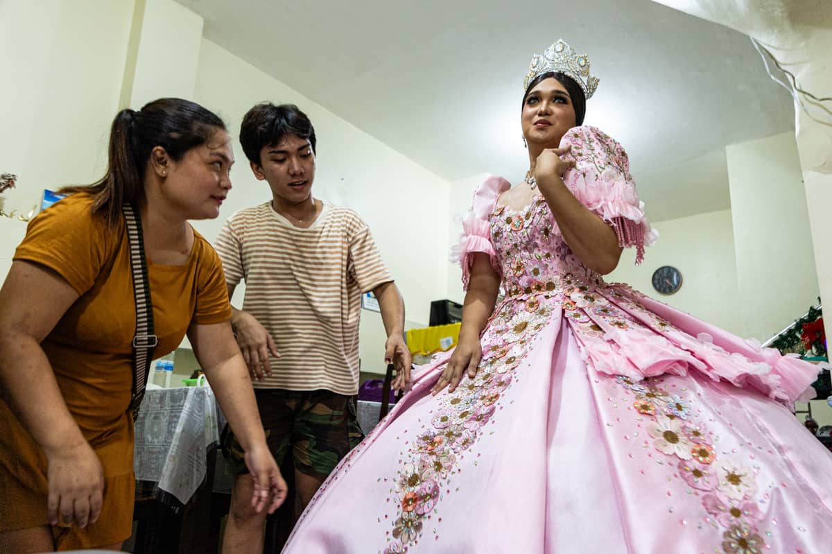 Andrei Cruz strikes a pose as his siblings Mikey and Ace Lawrence help him with his gown, ahead of the Sagayla procession.