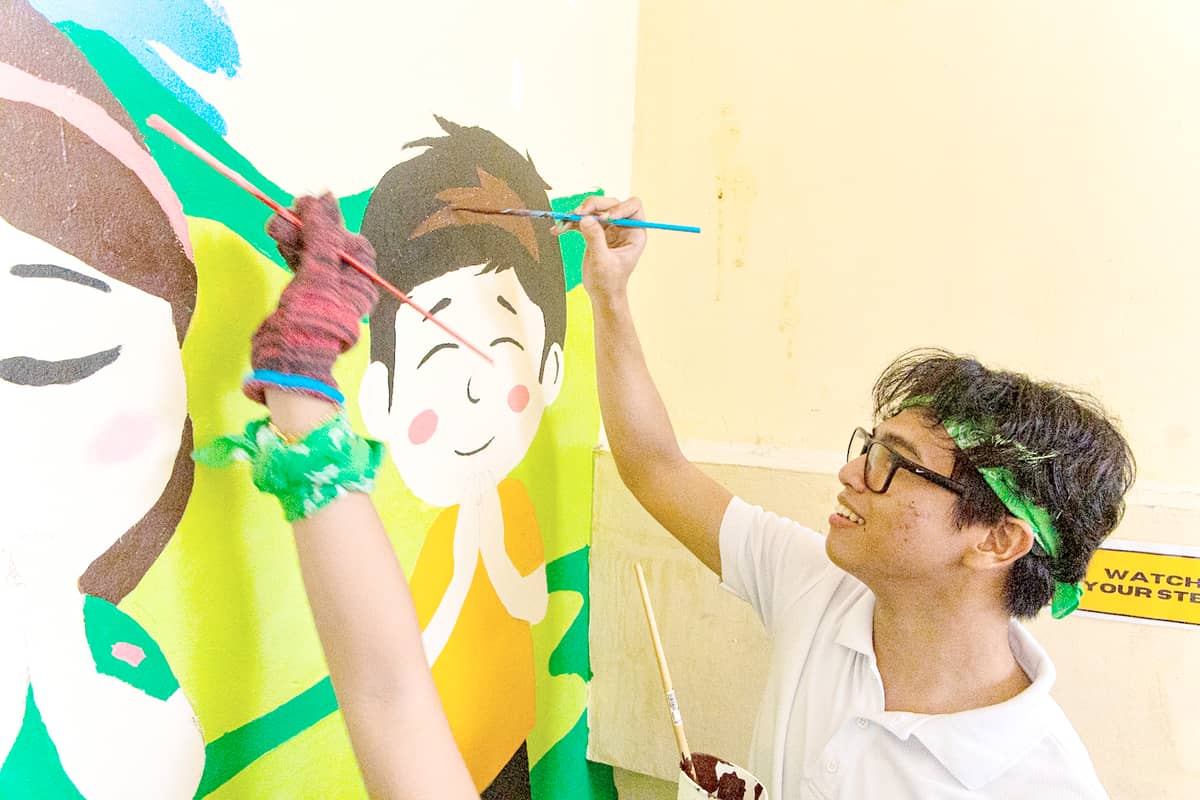 VOLUNTEERS from the Aboitiz Foundation Future Leaders Scholarship Program show the mural depicting the bayanihan tradition that they painted on a wall of the TSES as part of their Brigada Eskwela ’25 activity at the school in Quezon City.