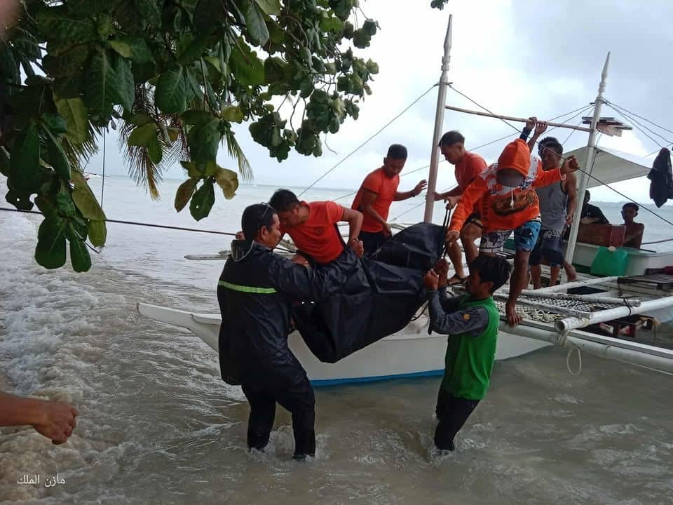 PERSONNEL assist in bringing ashore the body of a woman who died after a boat capsized off Balabac, Palawan during an unauthorized overseas voyage.