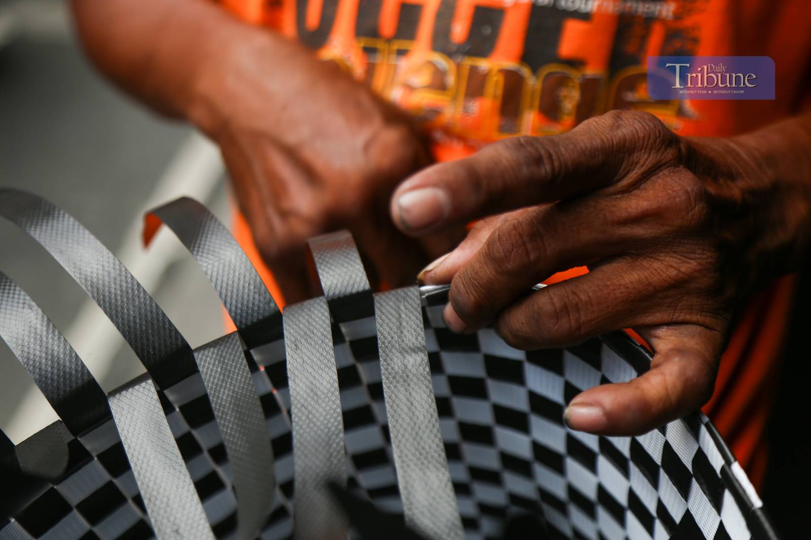 Roy Roja, 56, weaves "bayong" bags from recycled plastic baler straps along Recto Avenue in Manila on 26 June 2025. A native of Bulacan, Roja sells each handmade bayong for ₱250 and can complete up to three bags a day.