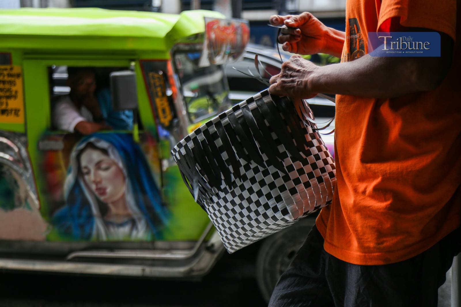 Roy Roja, 56, weaves "bayong" bags from recycled plastic baler straps along Recto Avenue in Manila on 26 June 2025. A native of Bulacan, Roja sells each handmade bayong for ₱250 and can complete up to three bags a day.