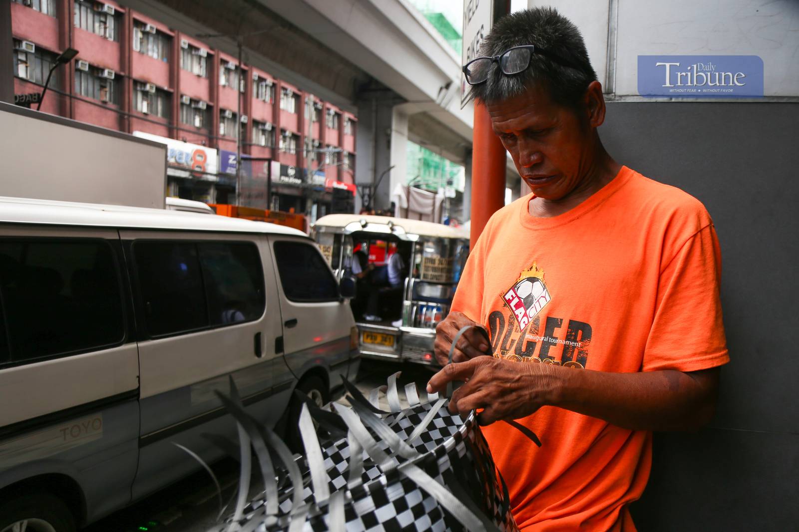 Roy Roja, 56, weaves "bayong" bags from recycled plastic baler straps along Recto Avenue in Manila on 26 June 2025. A native of Bulacan, Roja sells each handmade bayong for ₱250 and can complete up to three bags a day.
