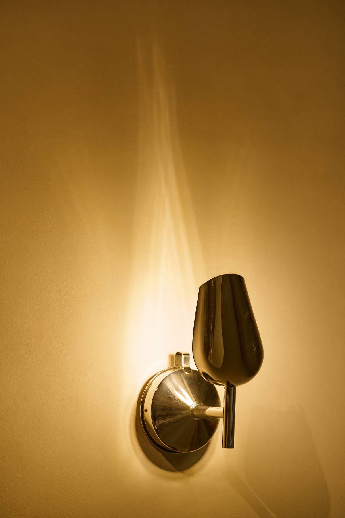 ‘Scoop Wall Light,’ crafted from stainless steel rice scoop and funnel, this sculptural fixture casts a warm glow reminiscent of a candlelight.