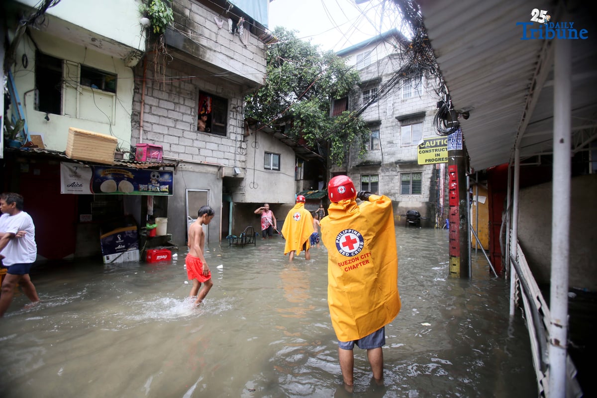Residents clear trash from knee-deep floodwaters outside their home in Roxas District, Quezon City, on Saturday, July 19, 2025, after continuous rains brought by the Habagat intensified by Severe Tropical Storm Crising. Red Cross personnel monitor the area.