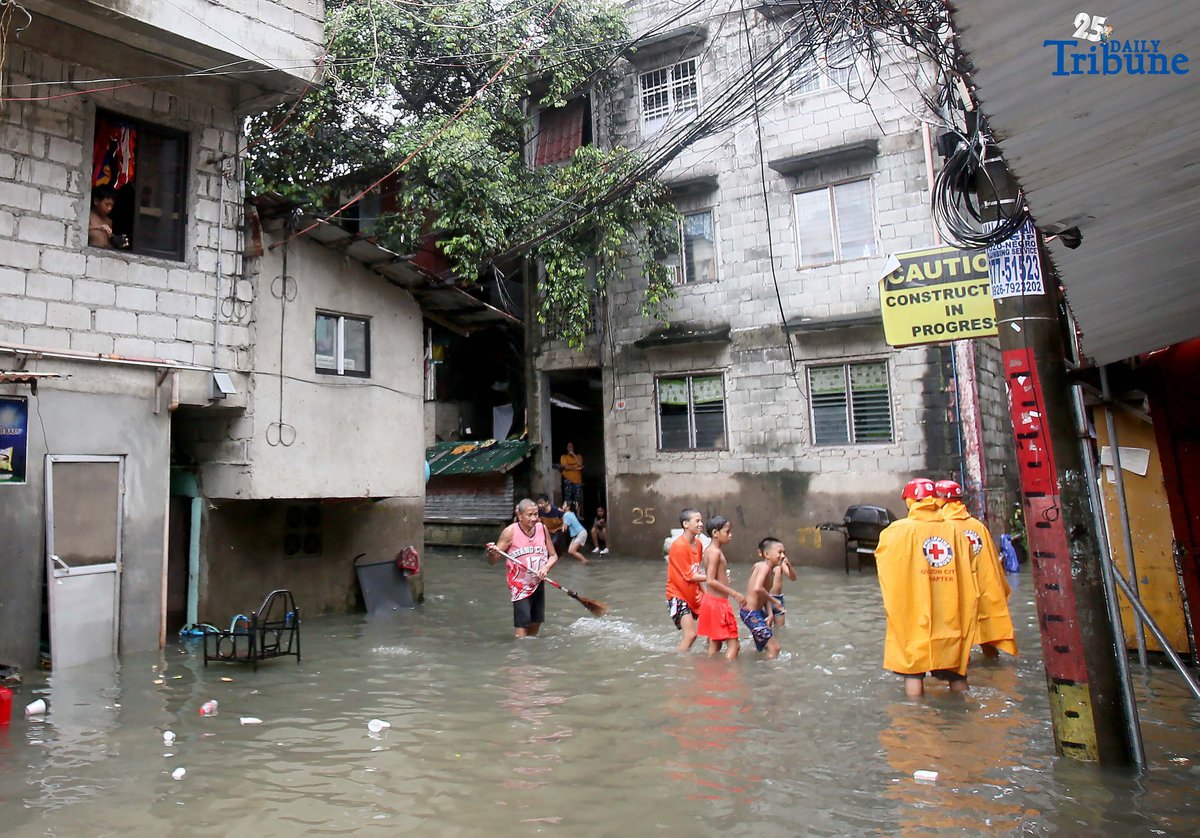 Residents clear trash from knee-deep floodwaters outside their home in Roxas District, Quezon City, on Saturday, July 19, 2025, after continuous rains brought by the Habagat intensified by Severe Tropical Storm Crising. Red Cross personnel monitor the area.