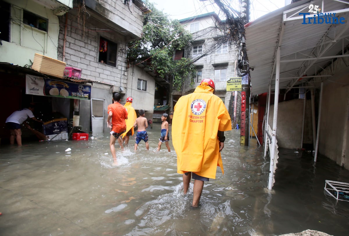 Residents clear trash from knee-deep floodwaters outside their home in Roxas District, Quezon City, on Saturday, July 19, 2025, after continuous rains brought by the Habagat intensified by Severe Tropical Storm Crising. Red Cross personnel monitor the area.