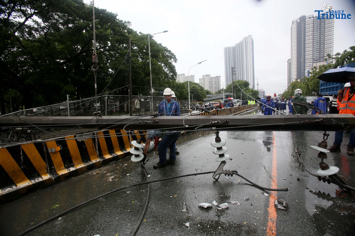 Personnel from Meralco, MMDA, and the Quezon City Police District work together to remove a fallen electric post along the northbound lane of Katipunan Avenue in Quezon City on Saturday, July 19, 2025. The post was knocked down by strong winds brought by the Habagat, intensified by Severe Tropical Storm Crising, around 11 a.m. Two vehicles reportedly crashed due to the incident.