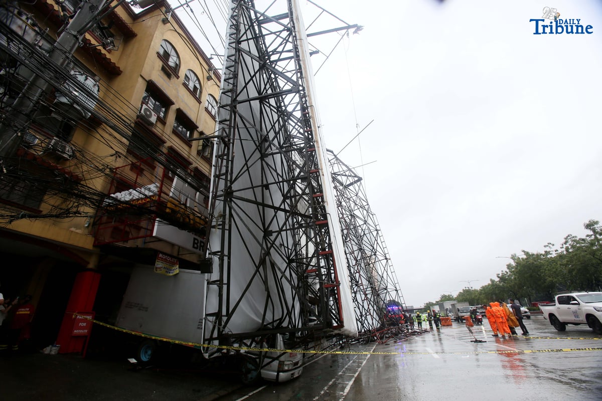 Bureau of Fire Protection personnel prepare to remove a collapsed billboard along the southbound lane of Katipunan Avenue in Quezon City on Saturday, July 19, 2025. The structure was toppled by strong winds around 11 a.m., brought by the Habagat intensified by Severe Tropical Storm Crising. Two vehicles reportedly crashed in the incident.