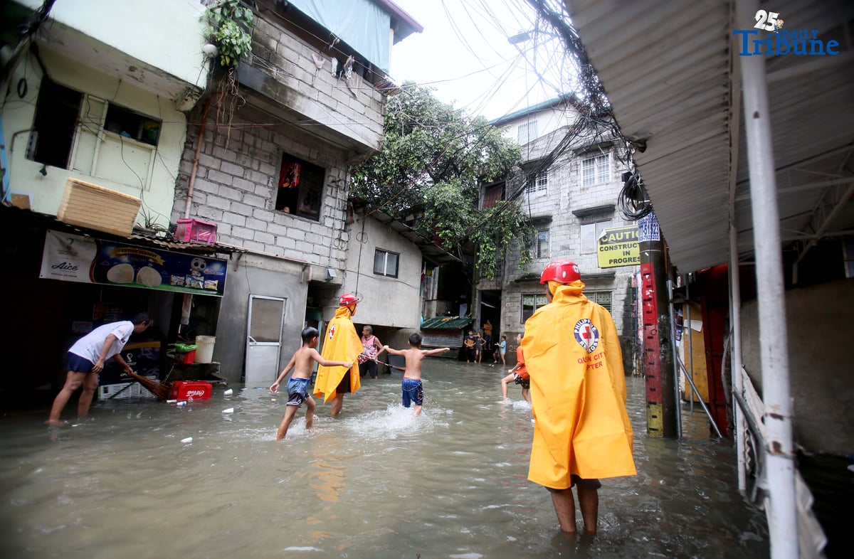Residents clear trash from knee-deep floodwaters outside their home in Roxas District, Quezon City, on Saturday, July 19, 2025, after continuous rains brought by the Habagat intensified by Severe Tropical Storm Crising. Red Cross personnel monitor the area.