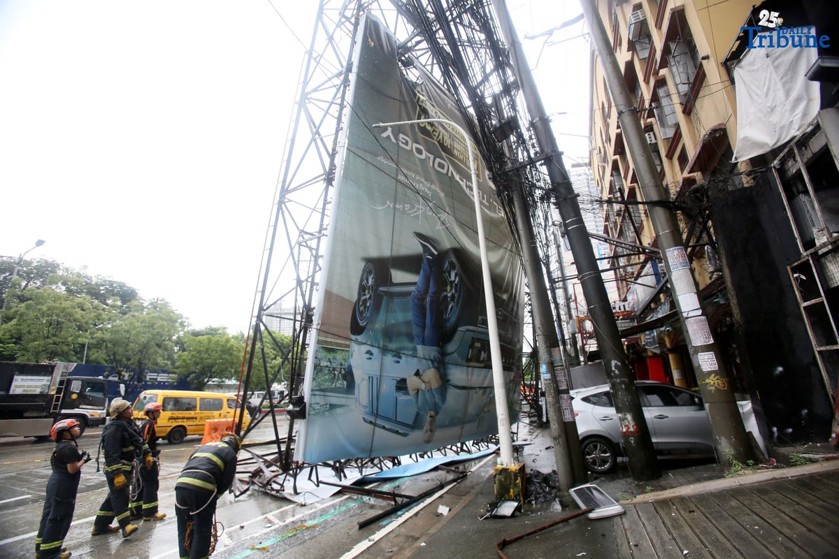 Bureau of Fire Protection personnel prepare to remove a collapsed billboard along the southbound lane of Katipunan Avenue in Quezon City on Saturday, July 19, 2025. The structure was toppled by strong winds around 11 a.m., brought by the Habagat intensified by Severe Tropical Storm Crising. Two vehicles reportedly crashed in the incident.