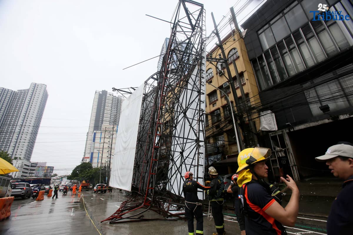 Bureau of Fire Protection personnel prepare to remove a collapsed billboard along the southbound lane of Katipunan Avenue in Quezon City on Saturday, July 19, 2025. The structure was toppled by strong winds around 11 a.m., brought by the Habagat intensified by Severe Tropical Storm Crising. Two vehicles reportedly crashed in the incident.