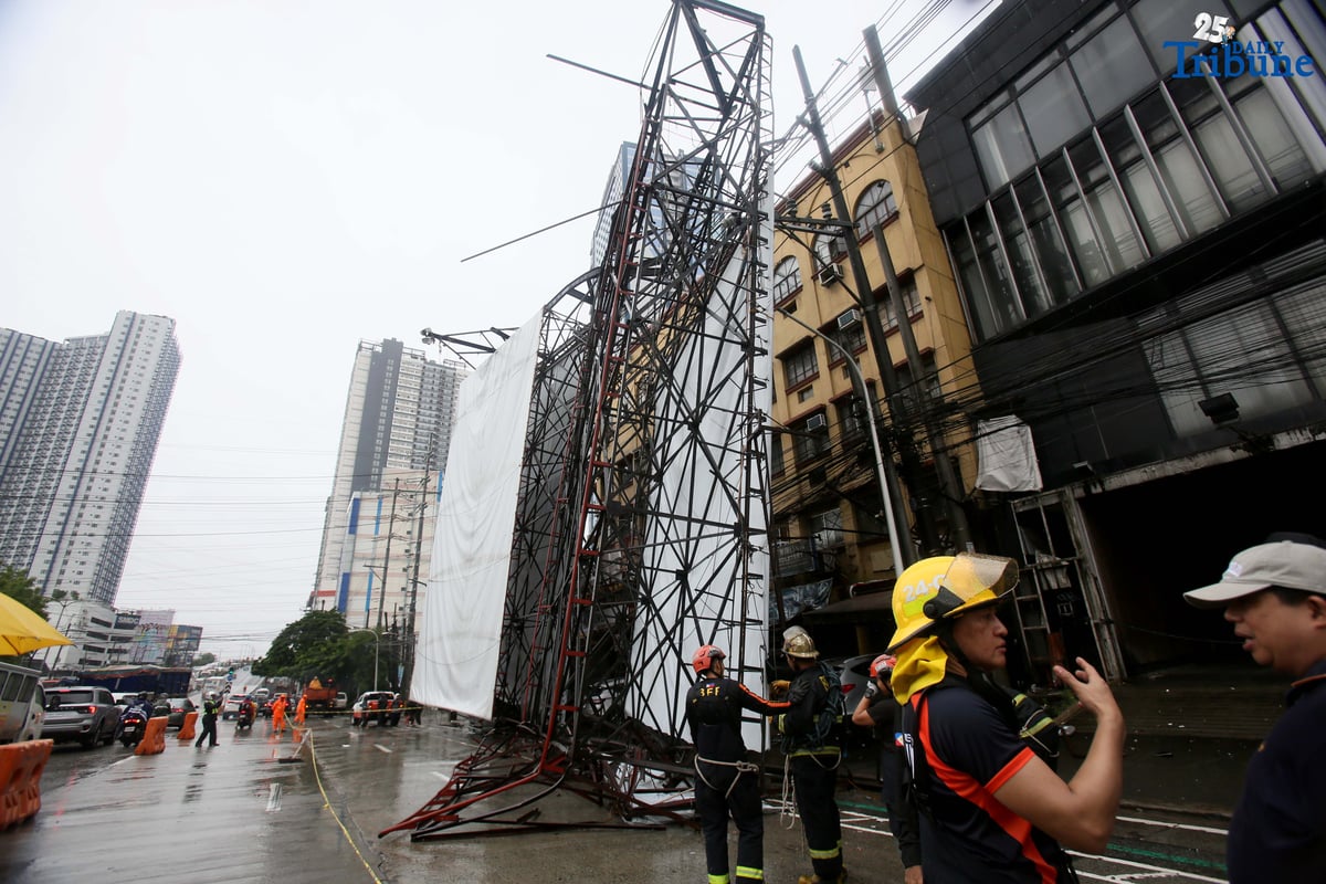 Bureau of Fire Protection personnel prepare to remove a collapsed billboard along the southbound lane of Katipunan Avenue in Quezon City on Saturday, July 19, 2025. The structure was toppled by strong winds around 11 a.m., brought by the Habagat intensified by Severe Tropical Storm Crising. Two vehicles reportedly crashed in the incident.