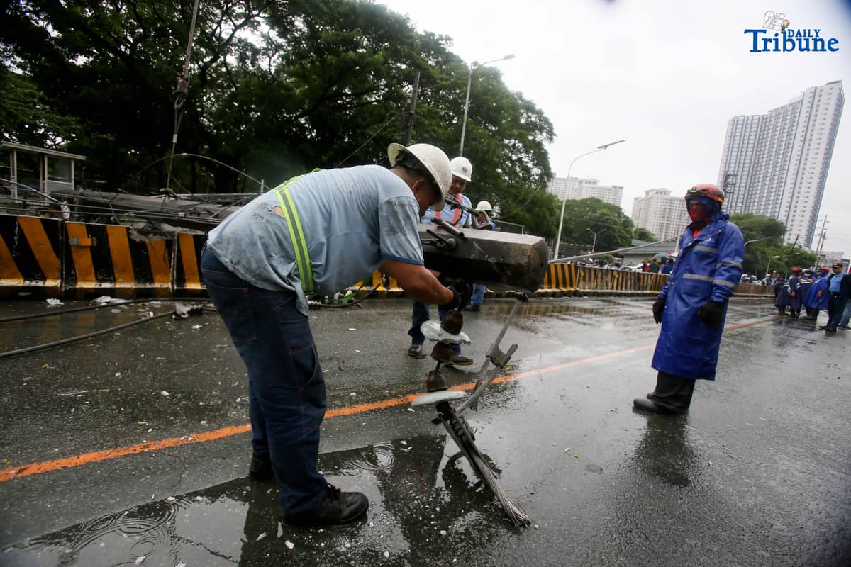 Personnel from Meralco, MMDA, and the Quezon City Police District work together to remove a fallen electric post along the northbound lane of Katipunan Avenue in Quezon City on Saturday, July 19, 2025. The post was knocked down by strong winds brought by the Habagat, intensified by Severe Tropical Storm Crising, around 11 a.m. Two vehicles reportedly crashed due to the incident.