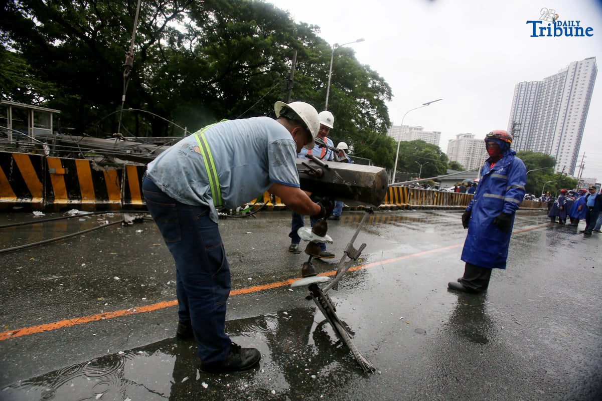 Personnel from Meralco, MMDA, and the Quezon City Police District work together to remove a fallen electric post along the northbound lane of Katipunan Avenue in Quezon City on Saturday, July 19, 2025. The post was knocked down by strong winds brought by the Habagat, intensified by Severe Tropical Storm Crising, around 11 a.m. Two vehicles reportedly crashed due to the incident.