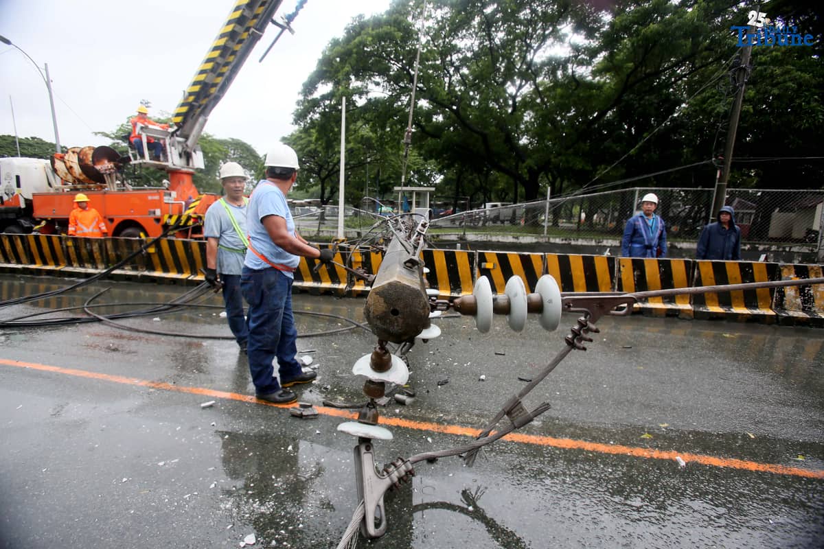 Personnel from Meralco, MMDA, and the Quezon City Police District work together to remove a fallen electric post along the northbound lane of Katipunan Avenue in Quezon City on Saturday, July 19, 2025. The post was knocked down by strong winds brought by the Habagat, intensified by Severe Tropical Storm Crising, around 11 a.m. Two vehicles reportedly crashed due to the incident.
