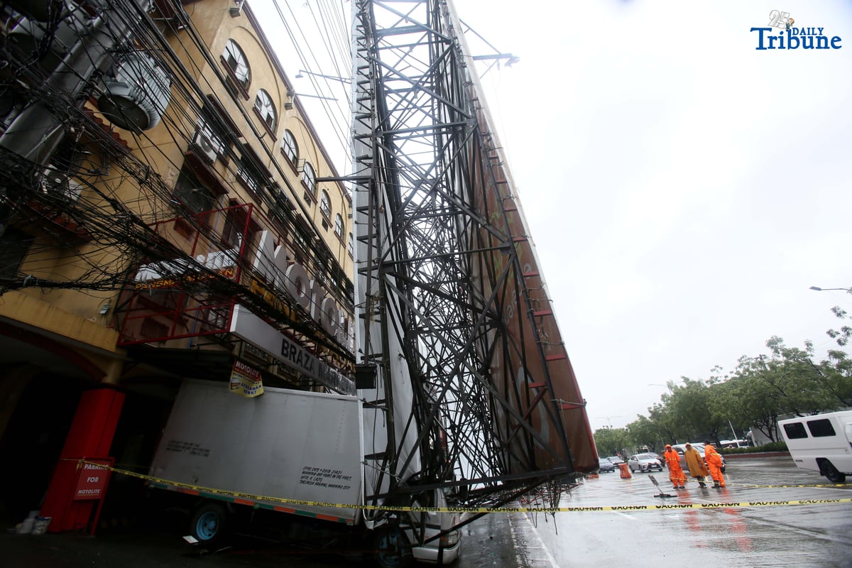 Bureau of Fire Protection personnel prepare to remove a collapsed billboard along the southbound lane of Katipunan Avenue in Quezon City on Saturday, July 19, 2025. The structure was toppled by strong winds around 11 a.m., brought by the Habagat intensified by Severe Tropical Storm Crising. Two vehicles reportedly crashed in the incident.