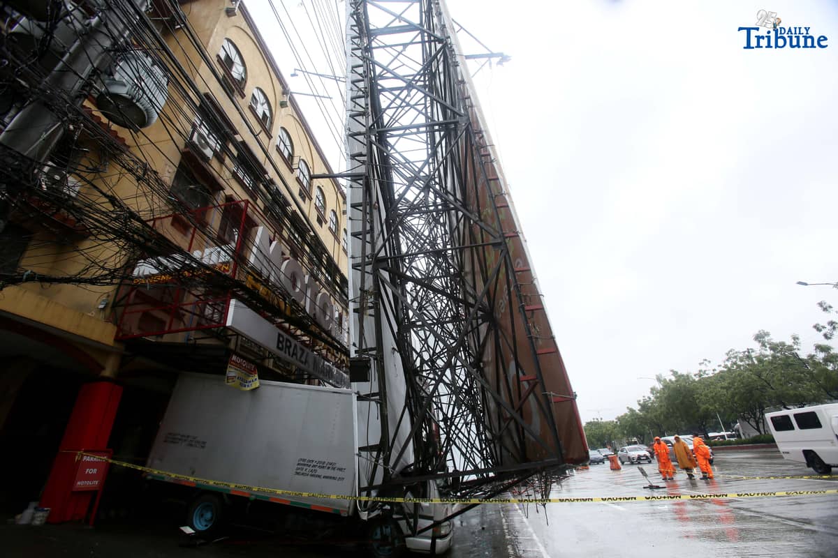 Bureau of Fire Protection personnel prepare to remove a collapsed billboard along the southbound lane of Katipunan Avenue in Quezon City on Saturday, July 19, 2025. The structure was toppled by strong winds around 11 a.m., brought by the Habagat intensified by Severe Tropical Storm Crising. Two vehicles reportedly crashed in the incident.