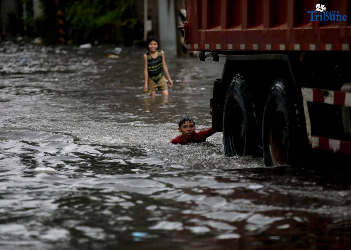 Children bathe and play in waist-deep floodwaters along Maria Clara Street in Quezon City on Saturday, 19 July 2025, following continuous rains from the Habagat, intensified by Severe Tropical Storm Crising.