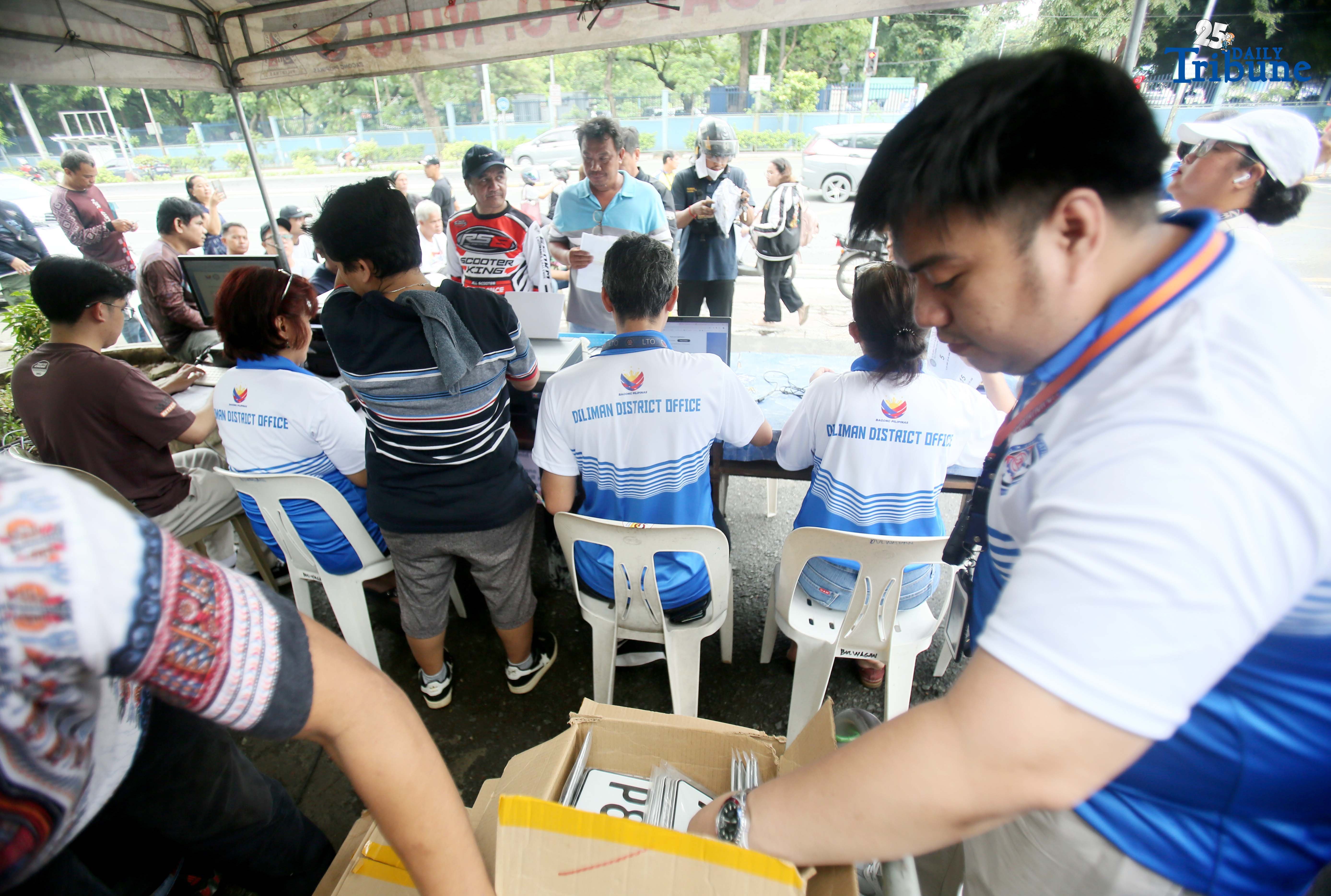 The Land Transportation Office Law Enforcement Unit assists motorcycle owners queuing for the LTO Palit Plaka program at the LTO main office along East Avenue in Quezon City on Saturday. The nationwide plate distribution program aims to address the backlog and ensure motorists comply with registration requirements.
