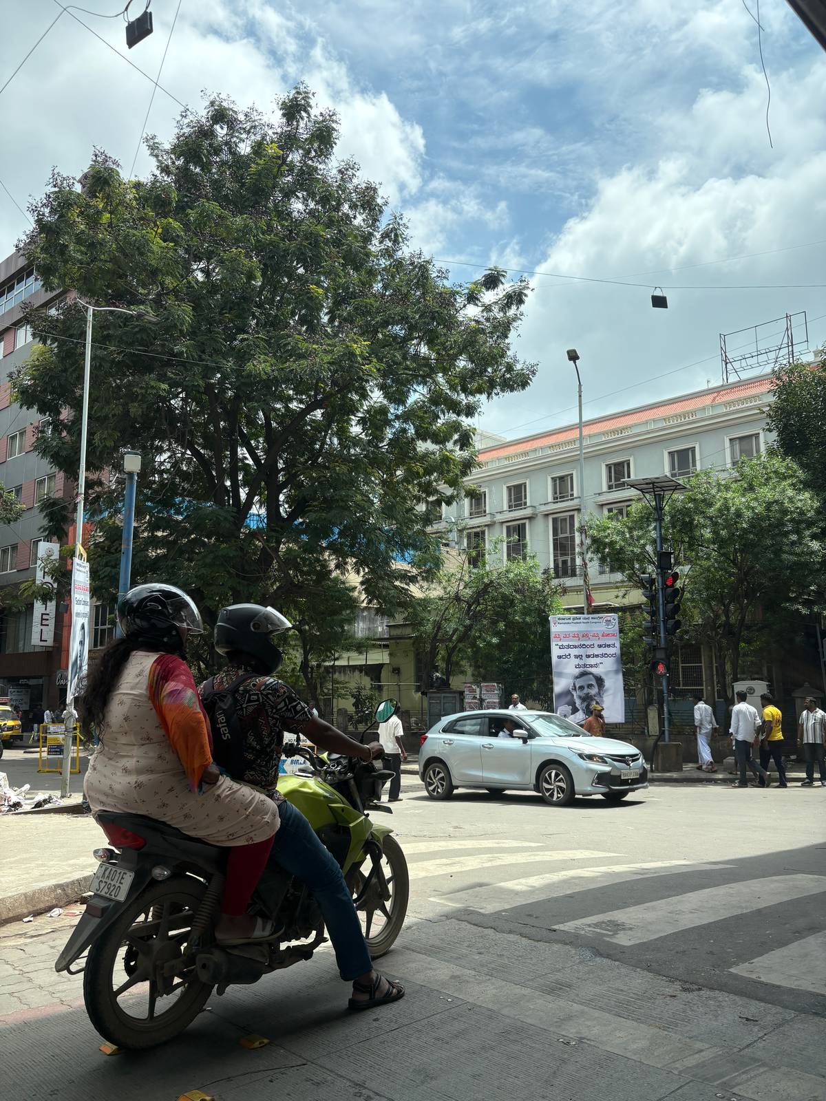 A COUPLE on a motorcycle pauses at a red light, capturing a quiet, shared moment amid the city’s hustle.