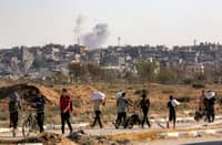 A smoke cloud erupts in the background from an explosion as people walk with bags of humanitarian aid they received at a distribution centre run by the US and Israeli-backed Gaza Humanitarian Foundation (GHF), as they cross the so-called "Netzarim corridor" in the central Gaza Strip, on August 22, 2025. The United Nations officially declared a famine in Gaza on August 22, the first time it has done so in the Middle East, with experts warning 500,000 people face "catastrophic" hunger. UN agencies have long been warning of the deteriorating humanitarian situation in Gaza, particularly as Israel steps up its offensive against Hamas.